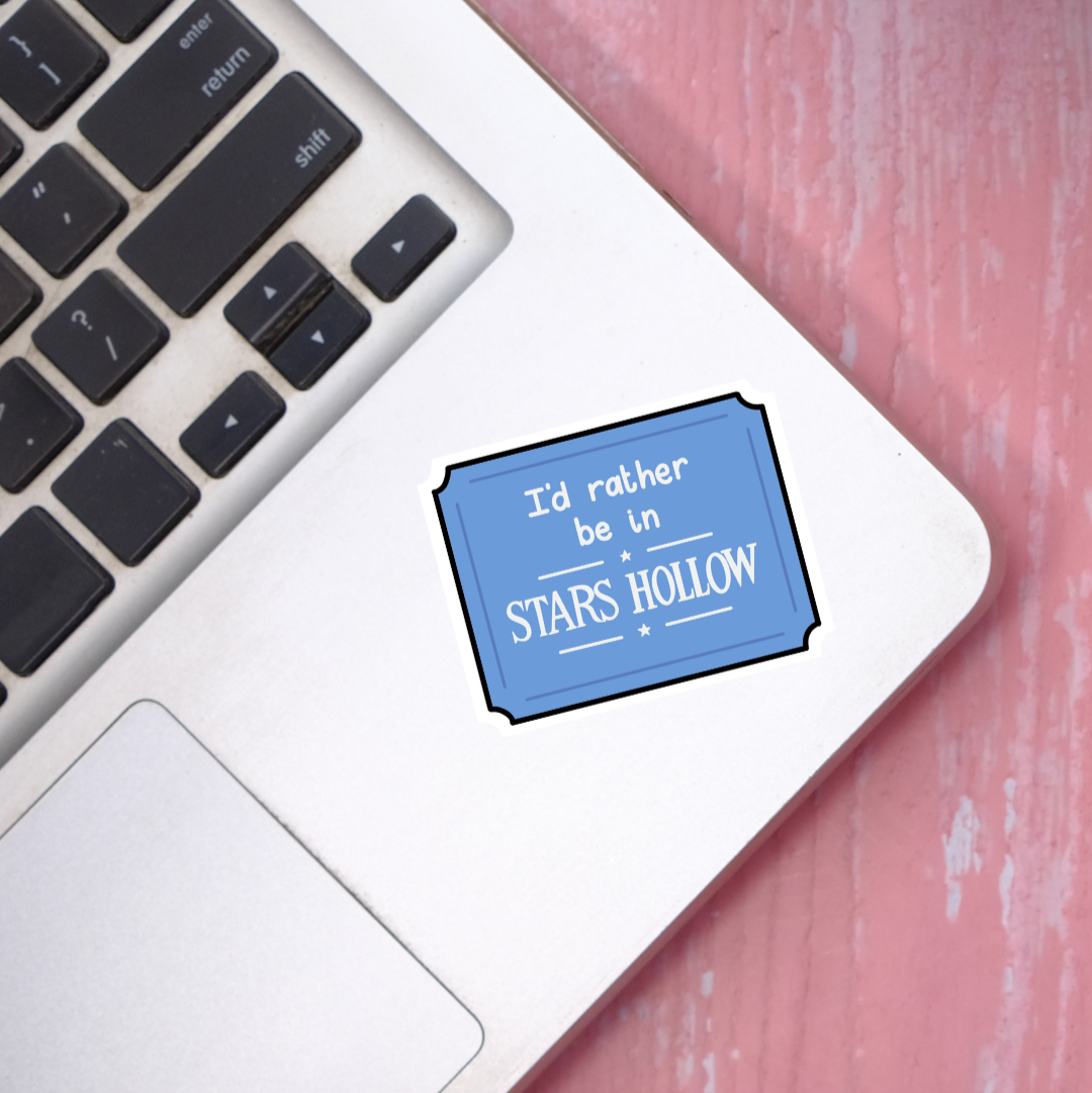 Blue sticker with text 'I'd rather be in Stars Hollow' on a laptop