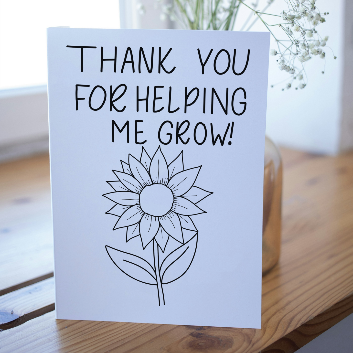 Card with 'Thank you for helping me grow!' text and a sunflower illustration on a wooden surface.