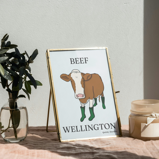 Framed picture of a cow with 'Beef Wellington' text on a table with a plant and candle.