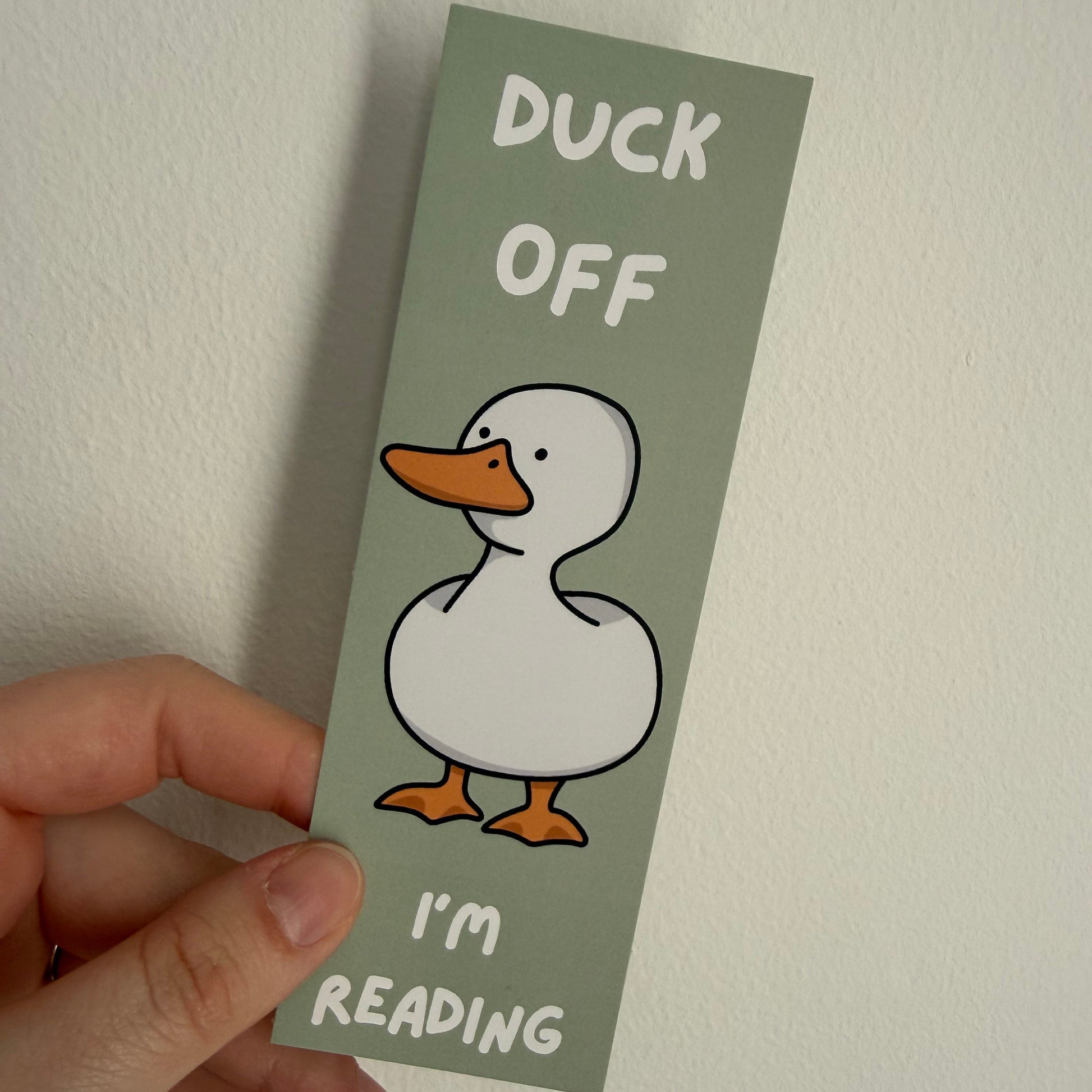 Bookmark with duck illustration and text held by a hand against a plain background