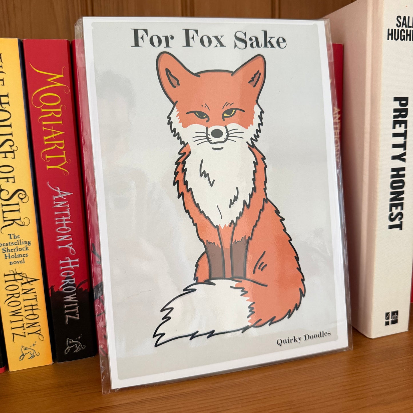 Stack of books with a fox illustration on one of them, on a wooden surface.