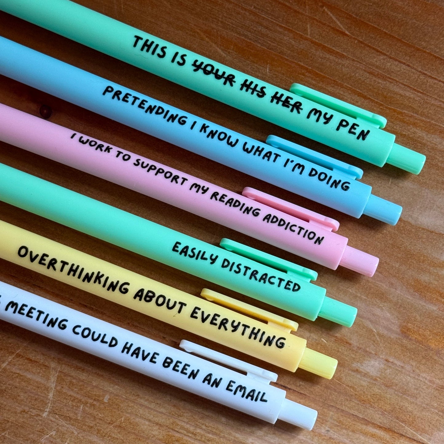 Set of colorful pens with humorous text on a wooden surface