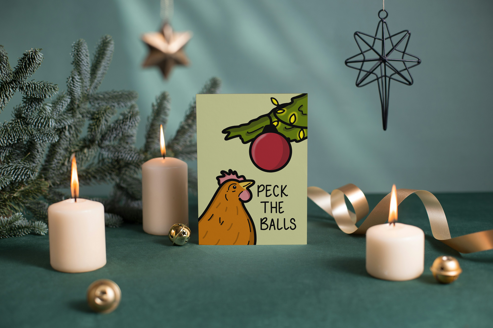 Card with a cartoon chicken and Christmas tree design, surrounded by candles and decorations on a green surface.