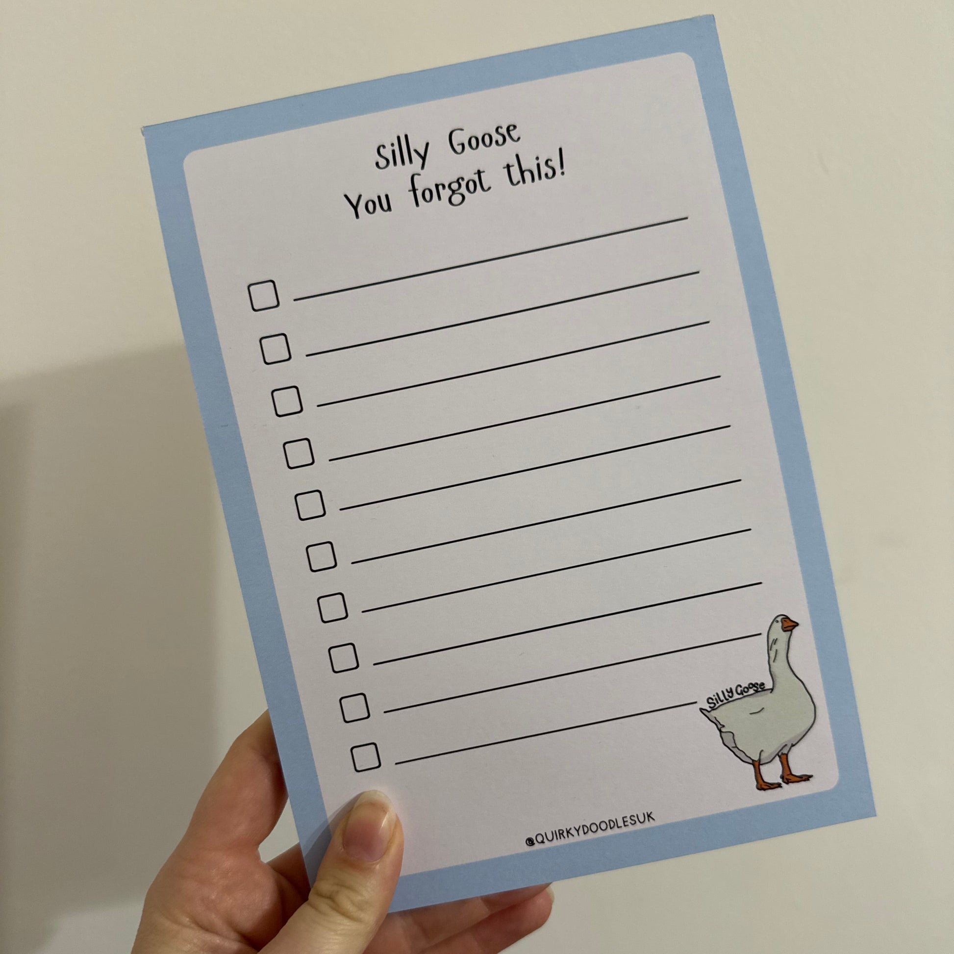 Hand holding a card with a list and illustration of a goose on a plain background
