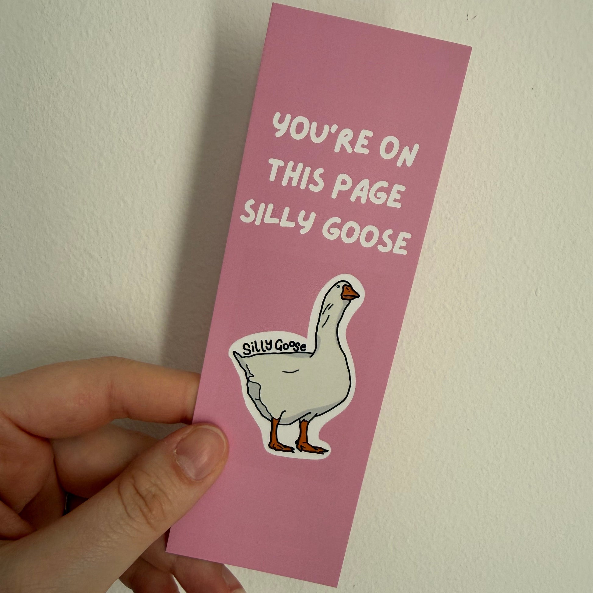 Pink bookmark with cartoon goose and text held by a hand against a white background
