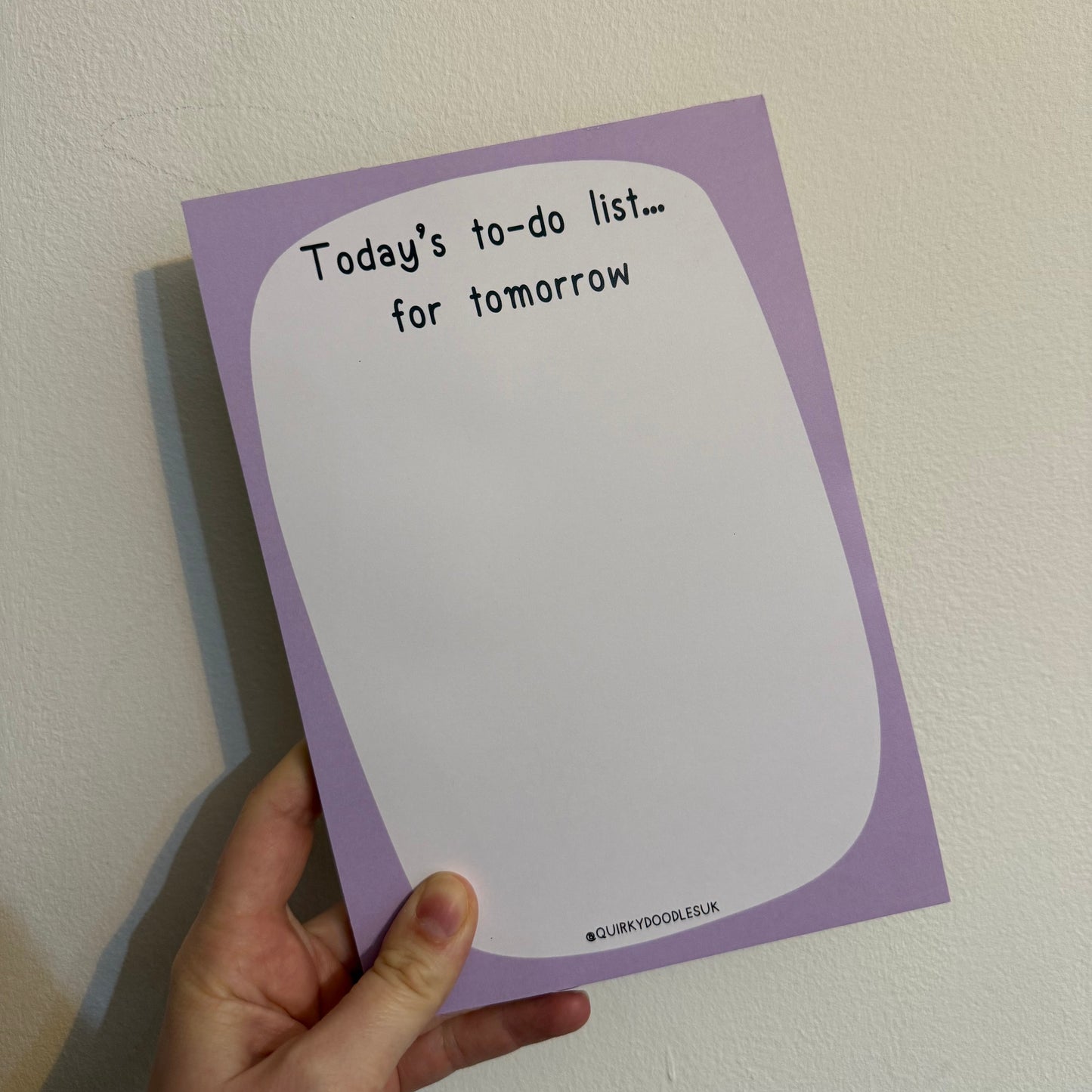 Hand holding a purple notepad with text on a plain background