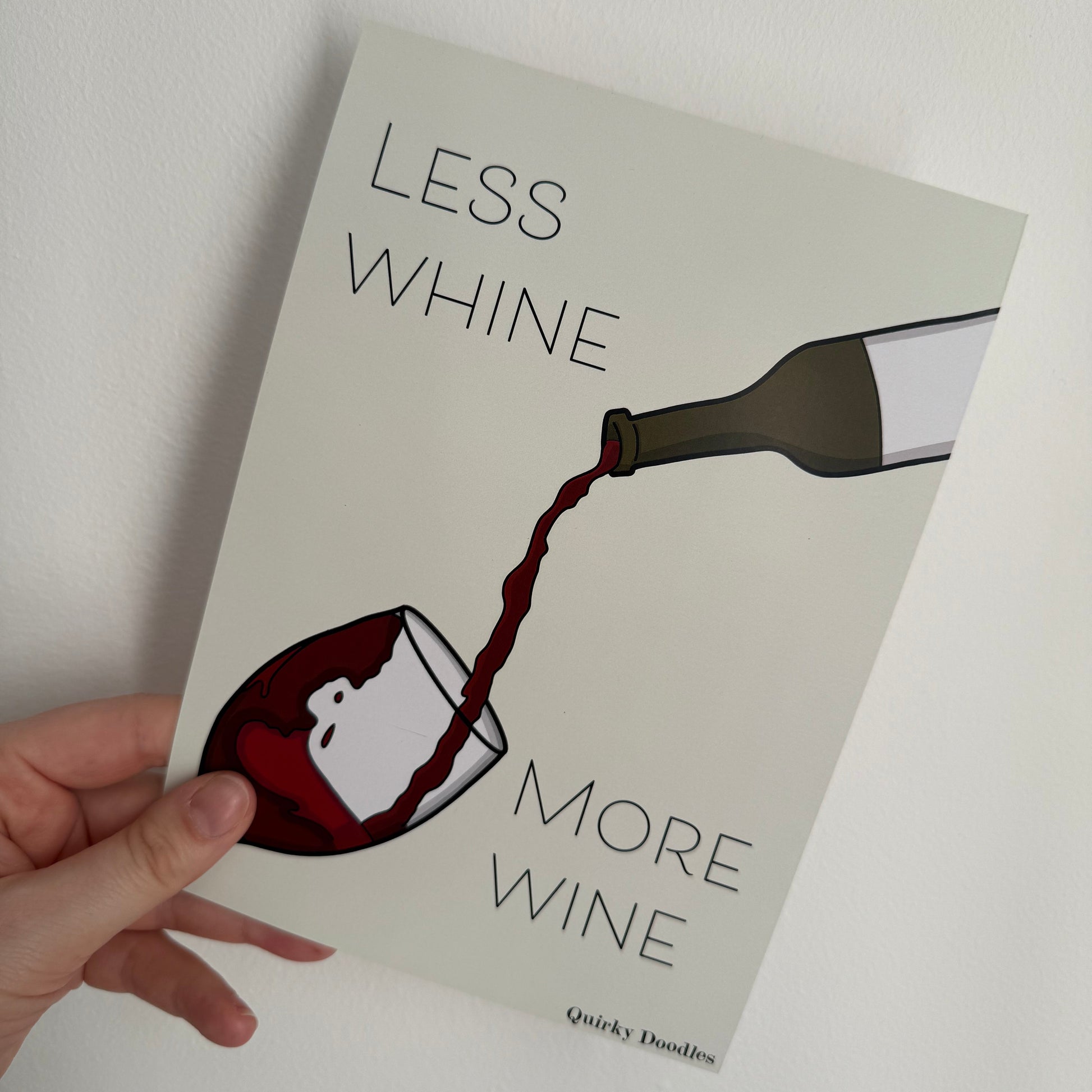 
Print titled 'Less Whine, More Wine' held by a hand on a white background